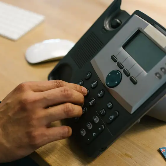 A hand dialing a desk phone beside a keyboard