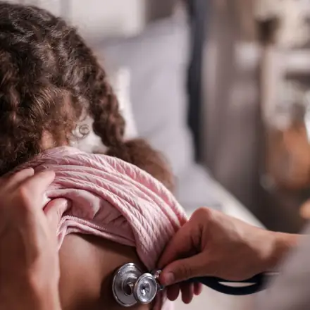 A doctor listening to a child’s back