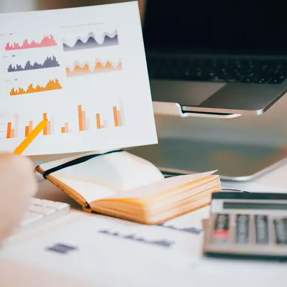 Hands analyzing charts beside a laptop