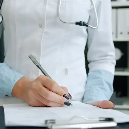 A physician signing paperwork on a clipboard