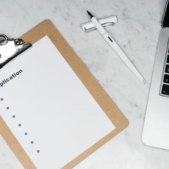 An application form on a clipboard beside a laptop