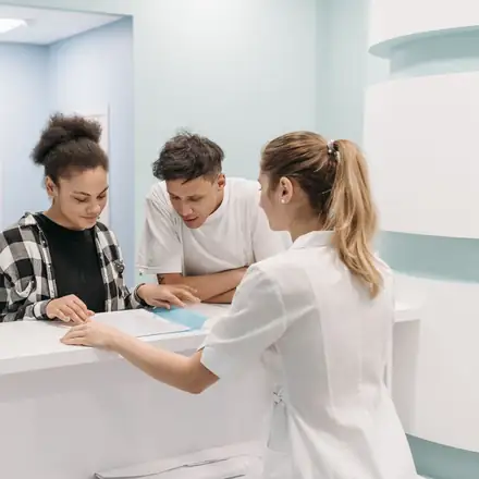 A nurse helping two patients at the front desk