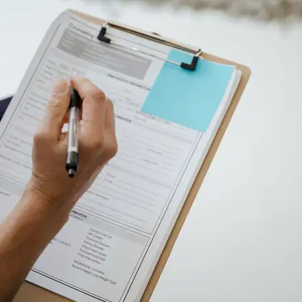 A hand filling in a form on a clipboard