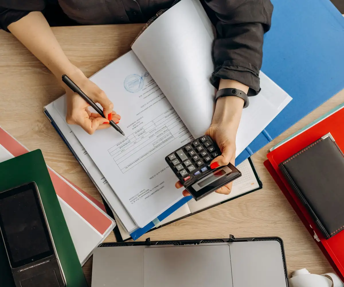 Hands working a calculator over open folders