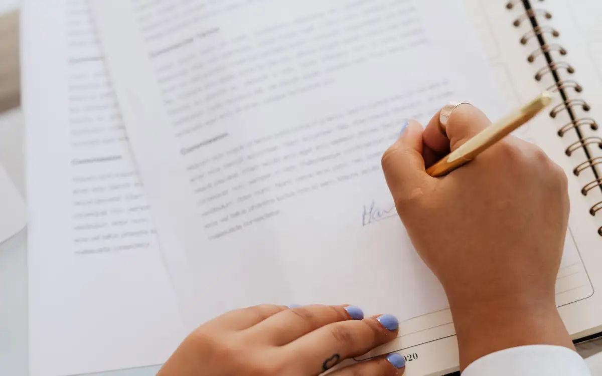 A hand writing on a document beside a notebook