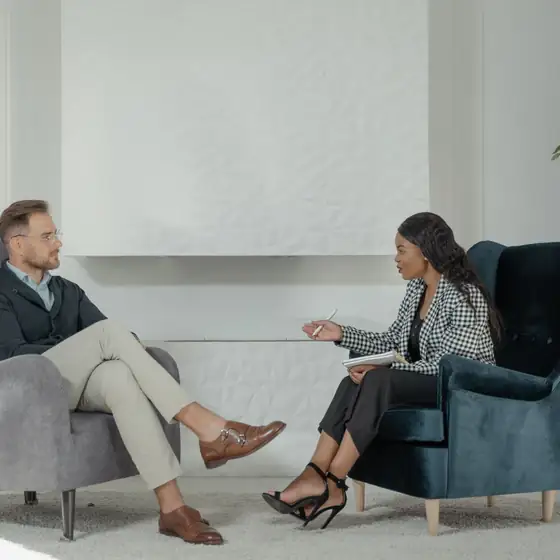 A therapist with a notebook talking with a client in armchairs