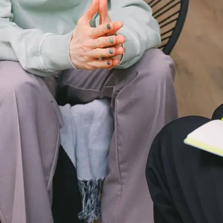 A client’s clasped hands across from a therapist holding a notebook