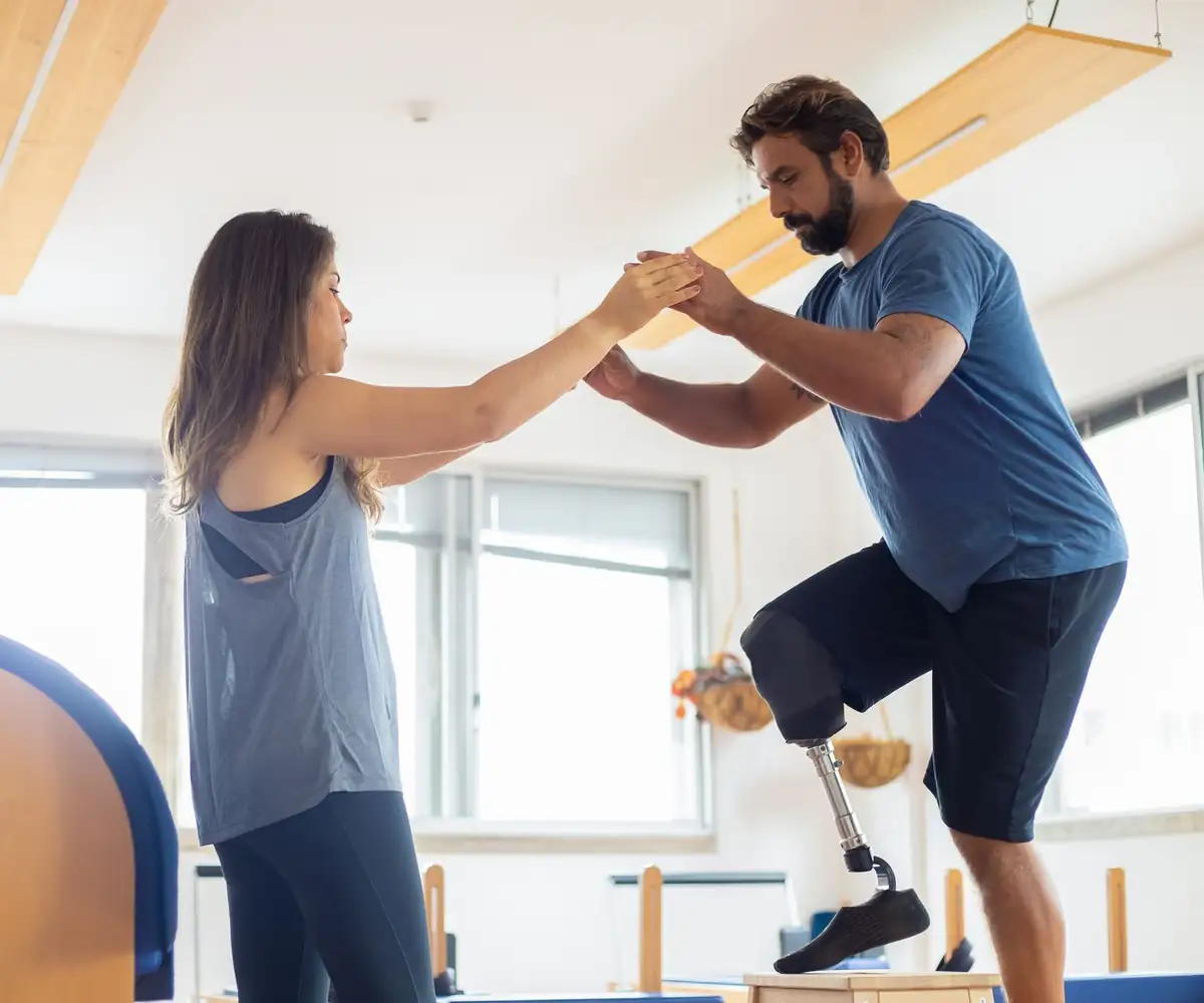 A physical therapist steadying a patient with a prosthetic leg through a balance exercise